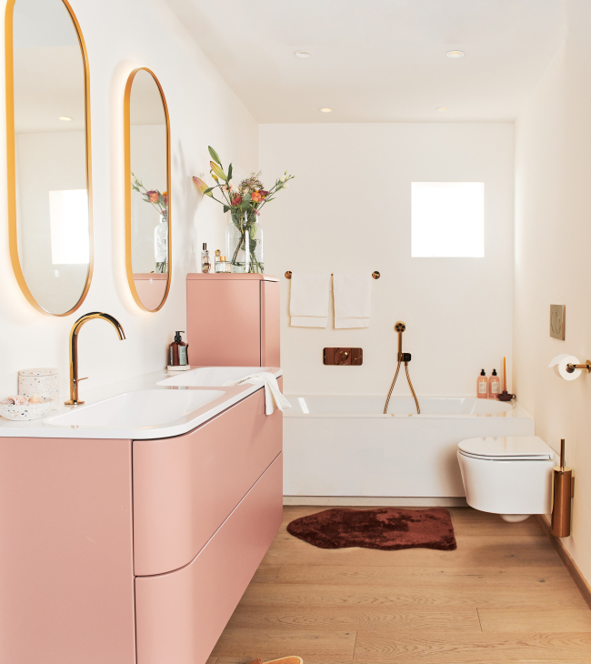 Kleine badkamer met roze kast, gouden kranen en ovalen spiegels